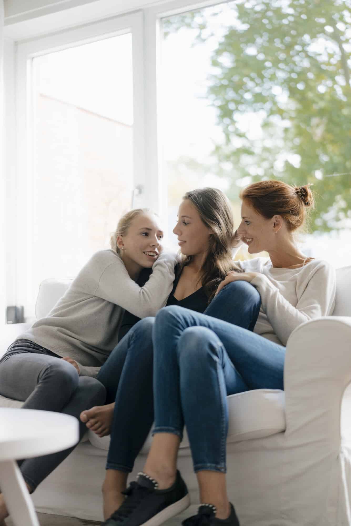 Happy mother with two teenage girls on couch at home