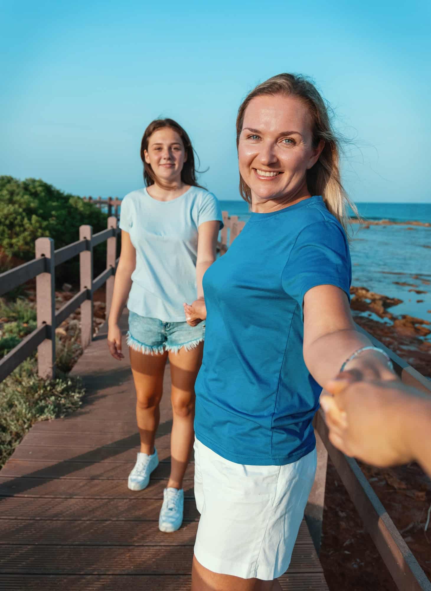 Mother and daughter running holding hands on by the sea at sunset